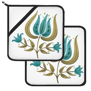 Puede incluir: Dos agarraderas blancas con borde negro. Cada agarradera presenta un diseño floral con flores y hojas de color turquesa y dorado. Las agarraderas son de forma cuadrada y tienen un lazo para colgar.