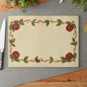 May include: Rectangular cutting board with a cream-colored surface. The board is framed with a decorative border of brown branches, green leaves, and red apples. A knife is visible on the left side.