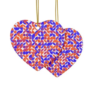 Op de afbeelding: Twee hartvormige keramische ornamenten met een geometrisch patroon van rode, blauwe en witte cirkels en halve cirkels.
