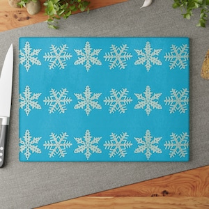 May include: A blue glass cutting board with a white snowflake pattern. The board is rectangular and has a smooth surface.