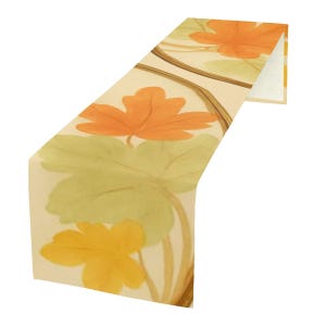 May include: A decorative table runner featuring a repeating pattern of orange, yellow, and green leaves on a cream background. The leaves are stylized and appear to be painted with watercolor. The runner is folded over, showing the underside.