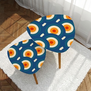 Op de afbeelding: Een set van twee nesttafels met een geometrisch patroon in blauw, wit en oranje. De tafels zijn driehoekig met afgeronde hoeken en hebben houten poten.