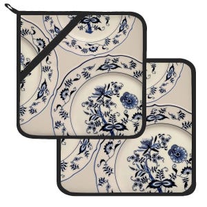 Può includere: Due presine per pentole con motivo blu e bianco con bordo nero. Il motivo presenta un design floreale con fiori e foglie blu su uno sfondo bianco.