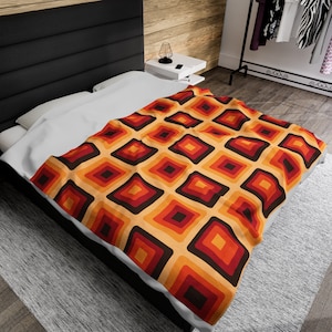 May include: A white bed with a brown, orange, and red geometric patterned duvet cover. The duvet cover has a repeating pattern of squares with different shades of brown, orange, and red.