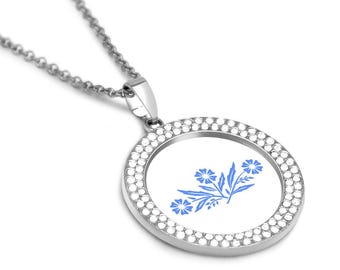 Puede incluir: Un collar de plata con un colgante redondo que presenta un diseño floral azul rodeado de diamantes de imitación transparentes.