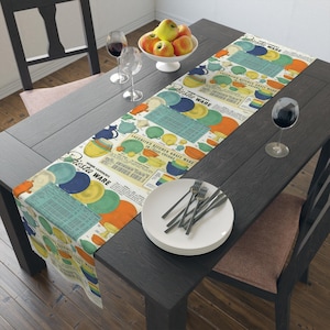 Può includere: Un runner da tavolo in stile vintage con un motivo colorato di piatti Fiesta Ware e un testo che recita "Homer Laughlin's Fiesta Ware in 5 Vivid Colors". Il runner è disposto su un tavolo in legno scuro con una ciotola di mele, bicchieri di vino e una mise en place con piatti bianchi e posate.