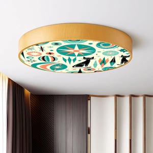 May include: A round flush mount ceiling light with a light wood grain finish. The light's interior features a retro design with teal, coral, and black geometric shapes and cat silhouettes. The light fixture is a decorative element.