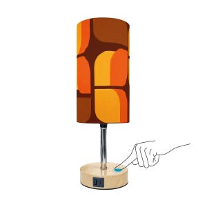 Peut inclure: Lampe de table cylindrique avec abat-jour à motifs rétro dans les tons marron, orange et jaune. La lampe a une tige chromée et une base en bois avec un port USB. Un doigt appuie sur le bouton d'alimentation.
