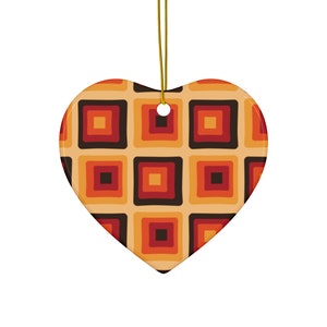 Op de afbeelding: Een hartvormige keramische ornament met een geometrisch patroon van vierkanten in tinten oranje, rood en bruin. De ornament heeft een gouden touwtje om op te hangen.