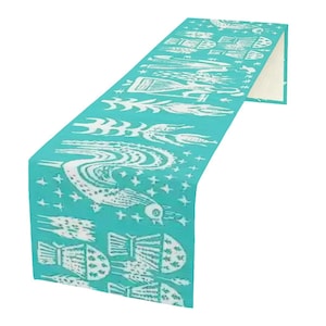 Peut inclure: Chemin de table turquoise avec un motif blanc répété d'oiseaux, de poissons et d'autres créatures aquatiques stylisées. Le chemin de table est plié, révélant un dessous de couleur crème. Le motif est imprimé sur le tissu.