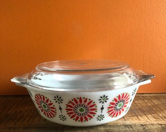 May include: White casserole dish with a glass lid. The dish has a red, green, and black floral pattern.