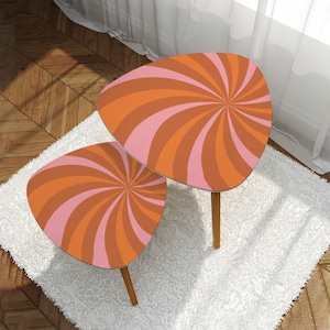 May include: A set of two nesting tables with a pink and orange swirl pattern. The tables are made of wood and have a modern design.