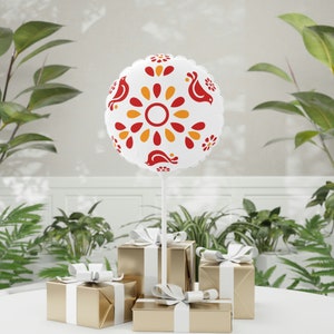 May include: A white balloon with a red and yellow floral pattern and small birds. The balloon is tied to a white string and is floating above three gold gift boxes with white ribbon.