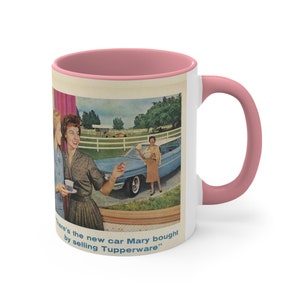 May include: A white ceramic mug with a pink rim and handle. The mug features a vintage advertisement with a blue car and three women. The text reads "There's the new car Mary bought by selling Tupperware."
