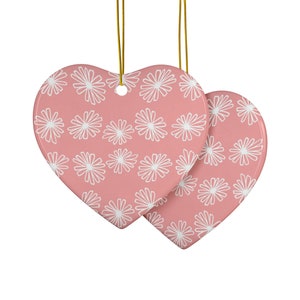Könnte beinhalten: Zwei rosafarbene herzförmige Keramik-Anhänger mit einem weißen Gänseblümchenmuster.