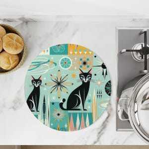Peut inclure: Un dessous de plat rond bleu sarcelle et blanc avec un motif rétro représentant deux chats noirs et des formes géométriques.