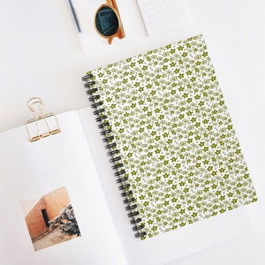 May include: A white spiral notebook with a green floral pattern. The notebook has a white background with small green flowers and dots.