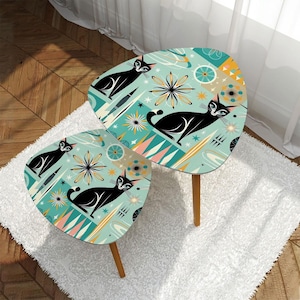 May include: A set of two nesting tables with a retro mid-century modern design. The tables feature a teal blue background with black cats, stars, and geometric shapes.