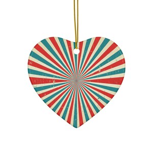 Op de afbeelding: Hartvormige ornament met een retro-ontwerp. Het ornament heeft een sunburst patroon in rood, blauwgroen en crème kleuren, met een distressed, vintage look. Een gouden draad is bevestigd om op te hangen. Ideaal voor vakantiedecoratie.