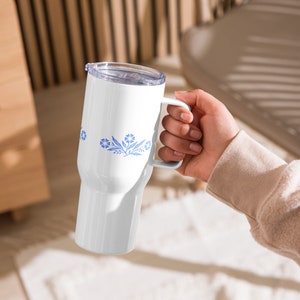 May include: White stainless steel travel mug with a blue floral design and a white handle.