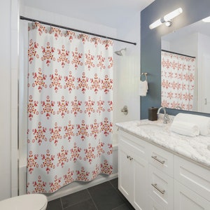 Pode incluir: Um cortina de chuveiro branco com um padrão floral vermelho e laranja. A cortina de chuveiro está pendurada em um banheiro com uma pia branca e um piso de azulejos cinza.