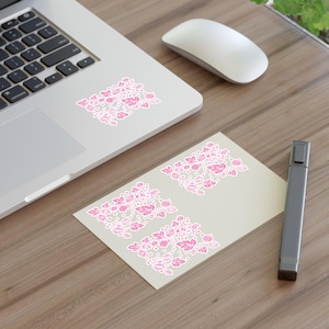 May include: Three pink and white floral stickers on a light brown wooden surface. The stickers feature a repeating pattern of pink flowers and leaves.
