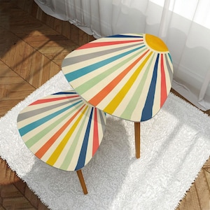 May include: A set of two nesting tables with a sunburst design in shades of blue, green, yellow, orange, and red. The tables have a rounded, oval shape and wooden legs.