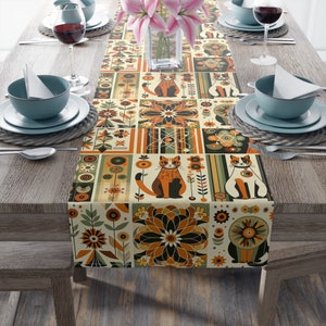 May include: A beige table runner with a geometric pattern featuring cats, flowers, and abstract shapes in shades of orange, green, and brown.