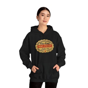 Könnte beinhalten: Schwarzer Kapuzenpullover mit einem goldenen und roten Logo mit der Aufschrift "Fire-King Heat-Proof Jade-ite Anchor Hocking Glass Co. Lancaster, Ohio, U.S.A."