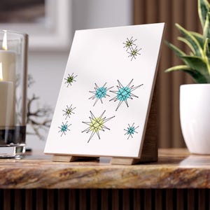 Peut inclure: Tuile en céramique blanche avec un design moderne du milieu du siècle, mettant en vedette des contours noirs d'étoiles avec des centres jaunes, bleus et verts.