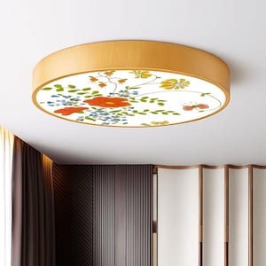 May include: A round flush mount ceiling light with a wooden frame. The light features a white center with a floral design in red, yellow, and blue. The flowers and leaves are arranged in a decorative pattern.