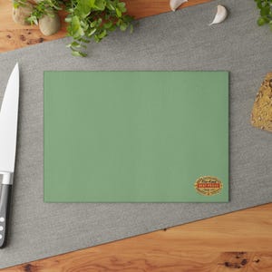 Puede incluir: Una tabla de cortar verde con una pegatina ovalada dorada que dice "Fire-King Heat-Proof Made in USA".