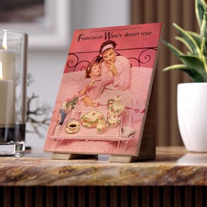 May include: A wooden framed print of a vintage magazine cover titled "Franciscan Ware's desert rose." The image depicts a woman and child in pink pajamas, with a breakfast tray featuring a teapot, teacups, and plates.