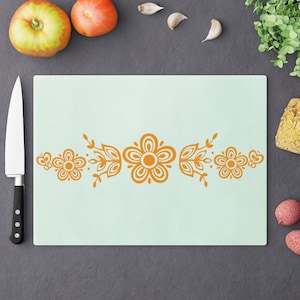 May include: A light blue cutting board with a decorative orange floral design. The design features stylized flowers and leaves.