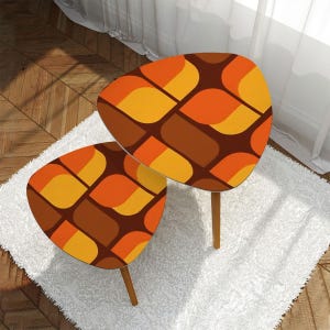 May include: Two nesting tables with a geometric pattern in shades of orange, brown, and yellow. The tables have a rounded, asymmetrical shape and wooden legs.