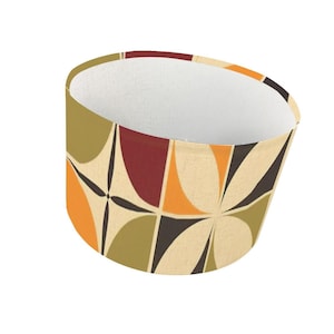 May include: A lampshade with a retro geometric pattern. The design features overlapping shapes in olive green, orange, burgundy, and black on a beige background. The interior is white.