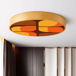 May include: A circular ceiling light with a light wood-effect frame. The interior has a retro design in orange, yellow, and brown. The light is mounted on a white ceiling. The diameter is approximately 60 cm.