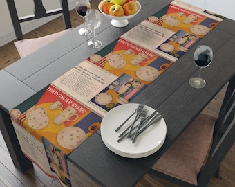 May include: A table runner with a vintage advertisement for "Princess Ware" featuring a colorful design of plates, cups, and a pitcher. The runner is on a dark wood table with a plate and silverware.