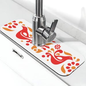 May include: A white sink protector with a decorative design featuring red and orange birds and floral elements. The protector is rectangular and sits beneath a stainless steel faucet.
