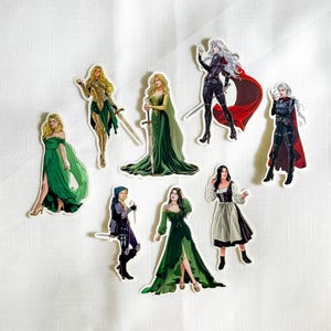 May include: A collection of eight die-cut stickers featuring illustrated figures in various outfits, including long green gowns, dark armor with red capes, and medieval-style clothing, with some figures holding swords or daggers in dynamic poses.