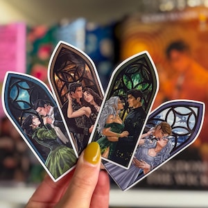 May include: Four decorative bookmarks with romantic illustrations of couples in gothic window frames. Each bookmark shows a different couple in various poses, with detailed artwork and vibrant colours. The bookmarks are held in a hand.
