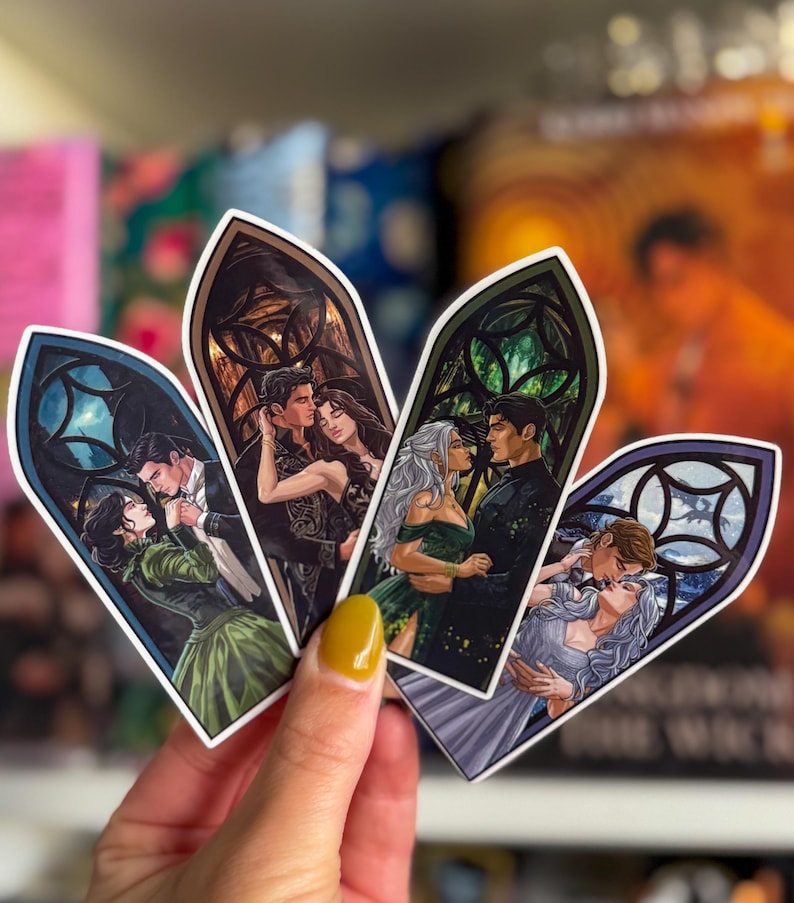 May include: Four decorative bookmarks with romantic illustrations of couples in gothic window frames. Each bookmark shows a different couple in various poses, with detailed artwork and vibrant colours. The bookmarks are held in a hand.