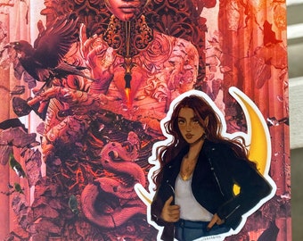 Op de afbeelding: Een levendige, artistieke print met een gedetailleerde illustratie van een vrouw met een raaf, en een sticker van een vrouw in een zwart jasje en jeans met een halve maan. Het kunstwerk is overwegend rood en oranje.