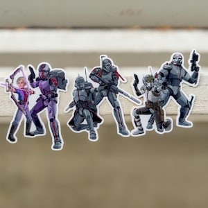 Puede incluir: Un conjunto de pegatinas troqueladas con personajes de una serie de animación de ciencia ficción. Las pegatinas muestran figuras en poses dinámicas, con armaduras y armas detalladas. La paleta de colores incluye tonos de gris, morado y rojo.