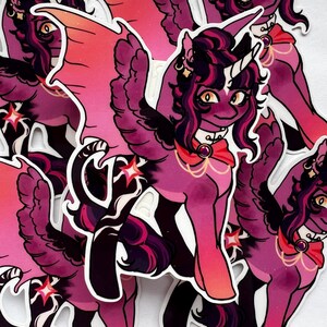 以下が含まれることがあります： 赤色のリボン、黒い羽根、金色の角を持つ、紫とピンクの漫画のユニコーンが描かれたステッカー4枚セット。ユニコーンは側面に星を持っており、ダイナミックなポーズで描かれている。