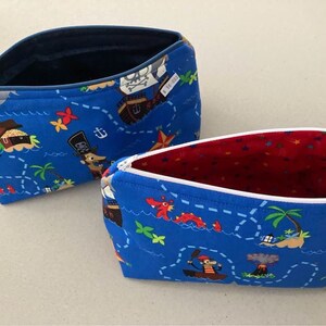 May include: Two blue zippered pouches with a pirate map design. The pouches feature a treasure map pattern with pirate ships, treasure chests, and palm trees. One pouch has a navy blue interior, and the other has a red interior.