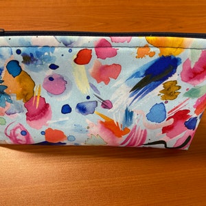 May include: A blue zippered pouch with a watercolour print of colourful abstract shapes and splashes.