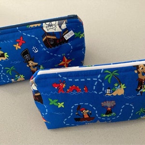 May include: Two blue zippered pouches with a pirate map design. The fabric features a treasure map with cartoon pirates, ships, treasure chests, and palm trees. One pouch has a blue zipper, and the other has a white zipper.