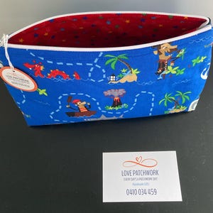 May include: A blue fabric zippered pouch with a pirate map design. The pouch features illustrations of pirates, islands, and sea creatures. The interior is red with a star pattern. A tag reads "LOVE PATCHWORK".