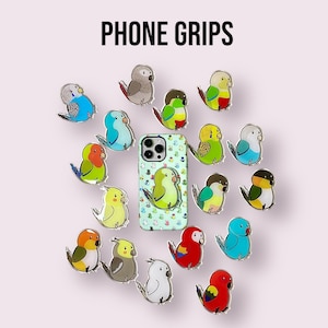 May include: A collection of bird-shaped phone grips and a phone case, all featuring bird designs. The text "PHONE GRIPS" is at the top. The grips and case are in various colours and patterns, creating a playful aesthetic. The background is a light pink.